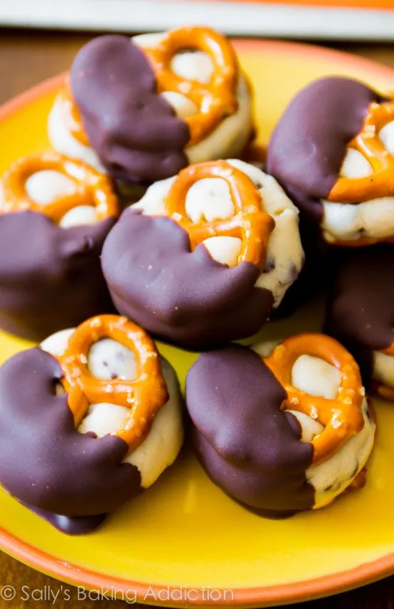 chocolate-dipped mini pretzel sandwiches filled with cookie dough, stacked on a yellow and orange plate.