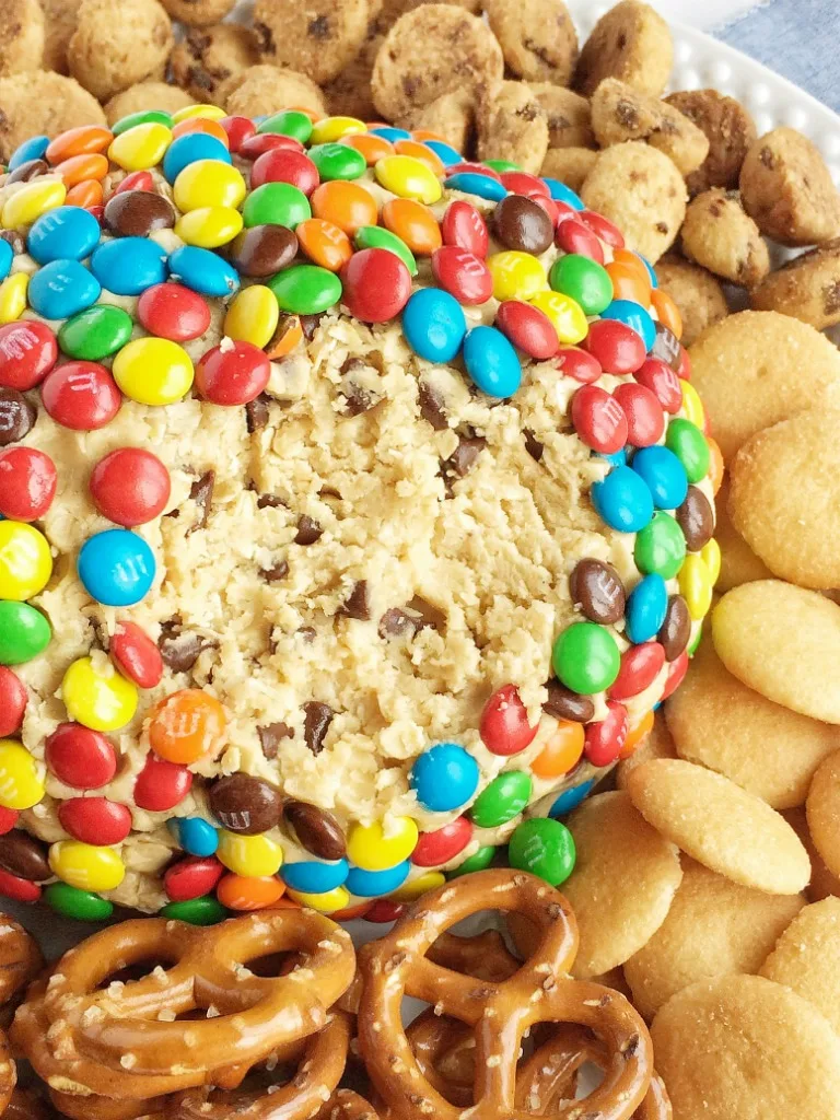 giant cookie dough cheeseball coated in m&ms, surrounded by mini cookies, pretzels, and wafers
