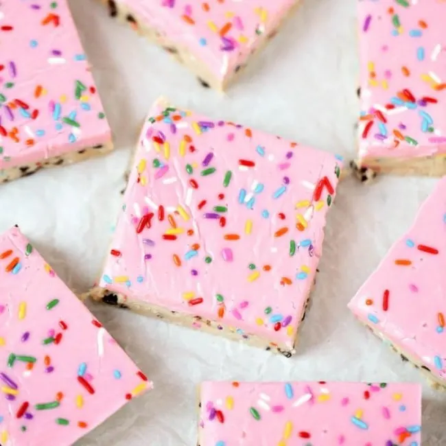 bright pink dessert bars with rainbow sprinkles cut into neat squares on parchment paper