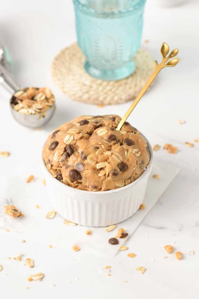 peanut butter oat mixture with chocolate chips in a white ramekin and gold spoon on a marble surface