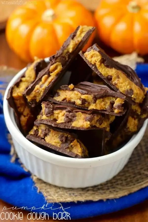 bark-style chocolate and pumpkin squares in a white bowl with small pumpkins in the background