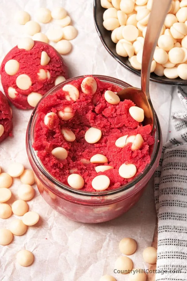 red velvet cookie dough with white chocolate chips in a jar and scoops on the side